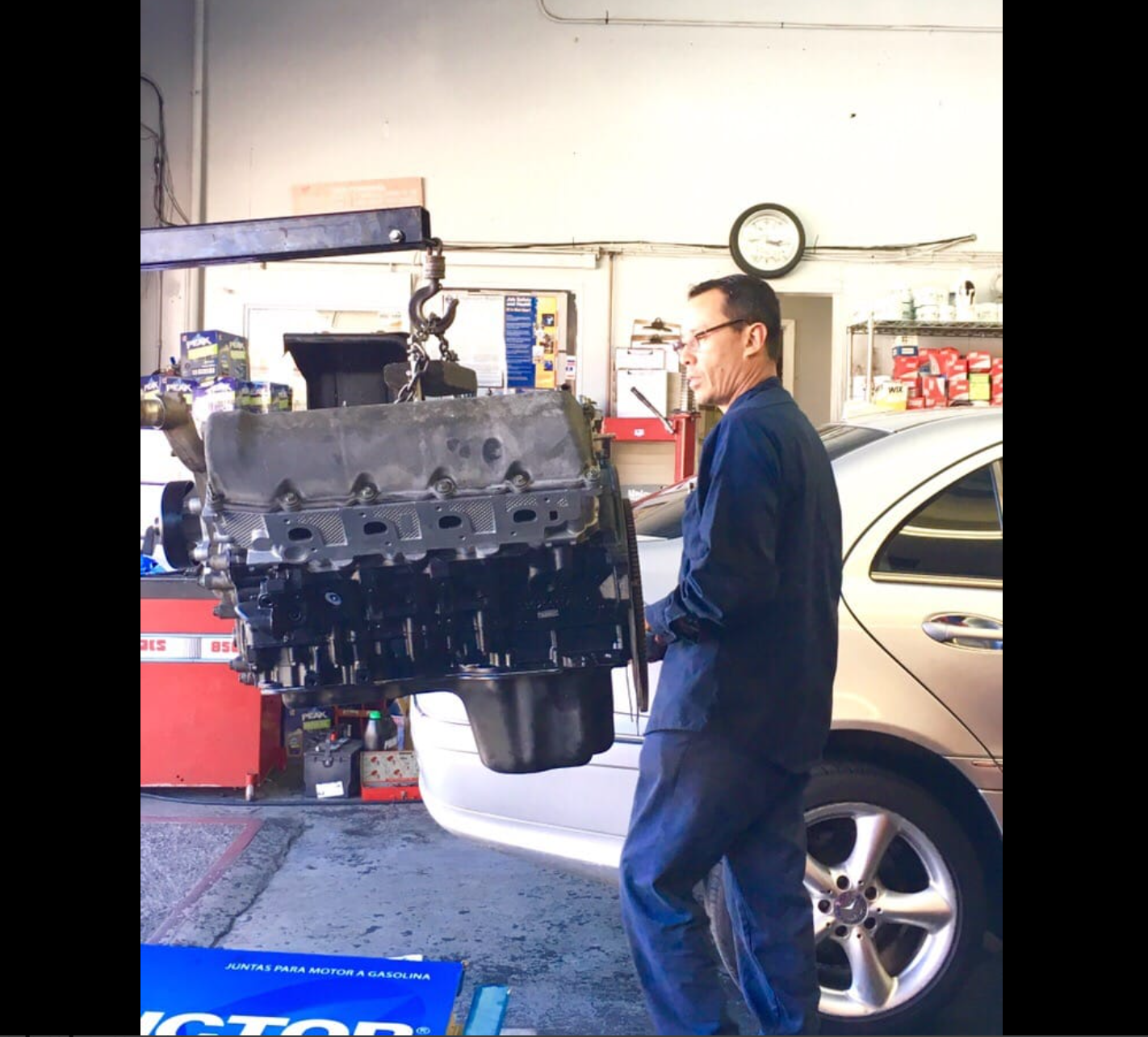 Technician moving an engine block beside a car inside Unique Automotive